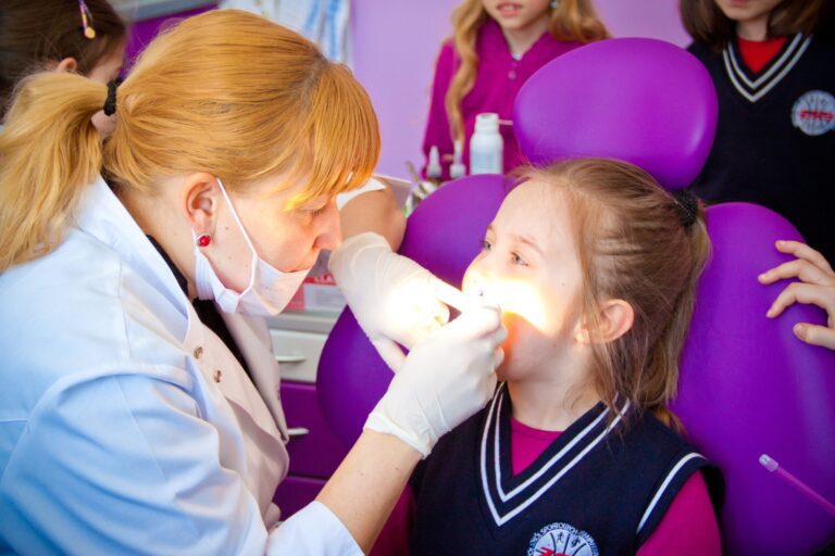 mała dziewczynka na fotelu dentystycznym z panią stomatolog wykonującą leczenie zębów